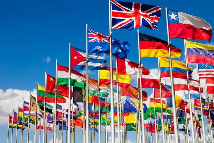 A group of international flags waving against a clear blue sky.