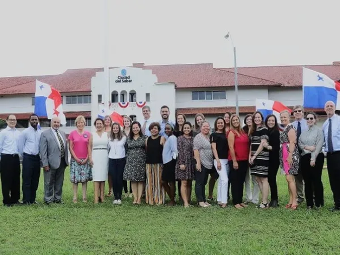 Group photo of people standing on grass in front of a building decorated with balloons.