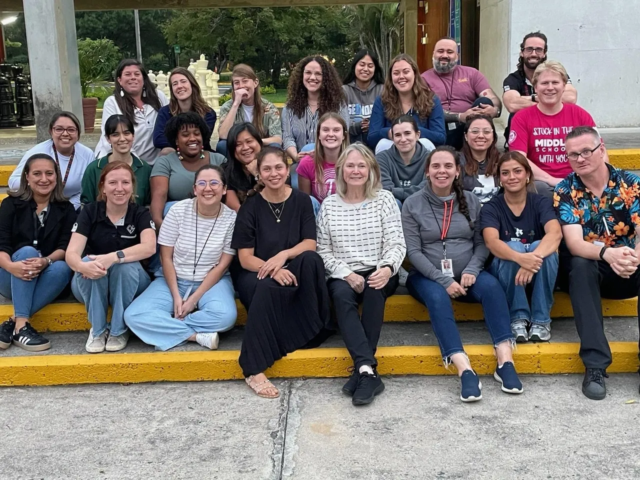 A diverse group of people sitting on steps outdoors, smiling and posing for a group photo.