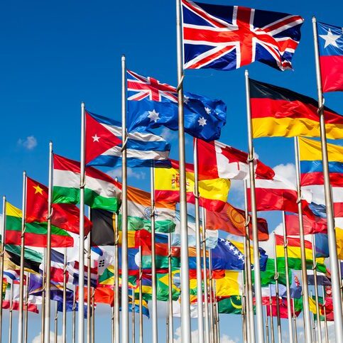 A group of international flags waving against a clear blue sky.